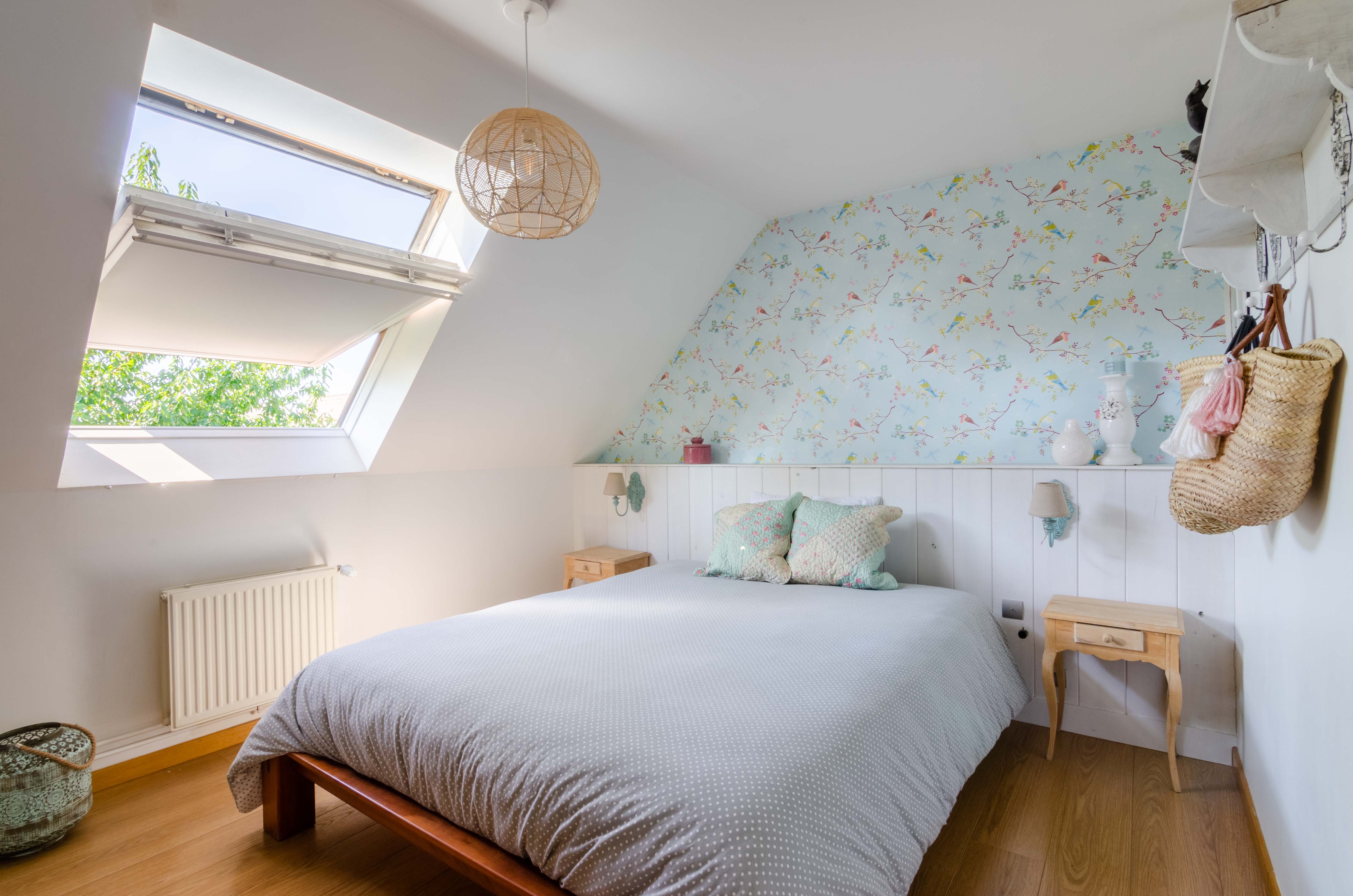 chambre mansardée avec papier peint à oiseaux sous un velux