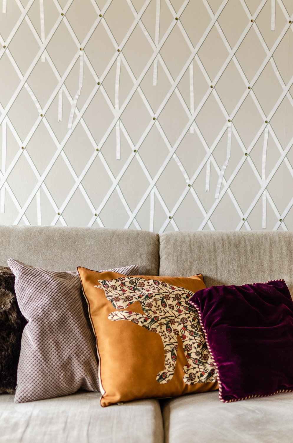 coussins colorés sur canapé beige devant un papier peint à losanges